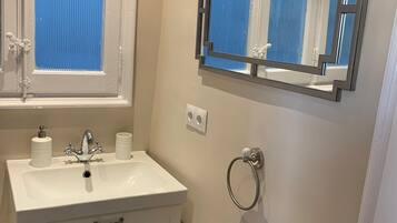 Un baño con tocador blanco, espejo y ventana con persianas azules.
