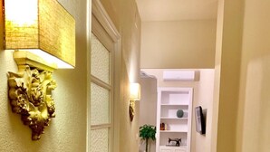 A hallway with a wooden parquet floor, white walls, a decorative wall sconce, a potted plant, and a white cabinet with a television mounted on the wall. - Hi Valencia Cánovas (Valencia)