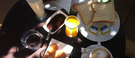 A breakfast table with croissants, toast, juice, jam, butter, and coffee.