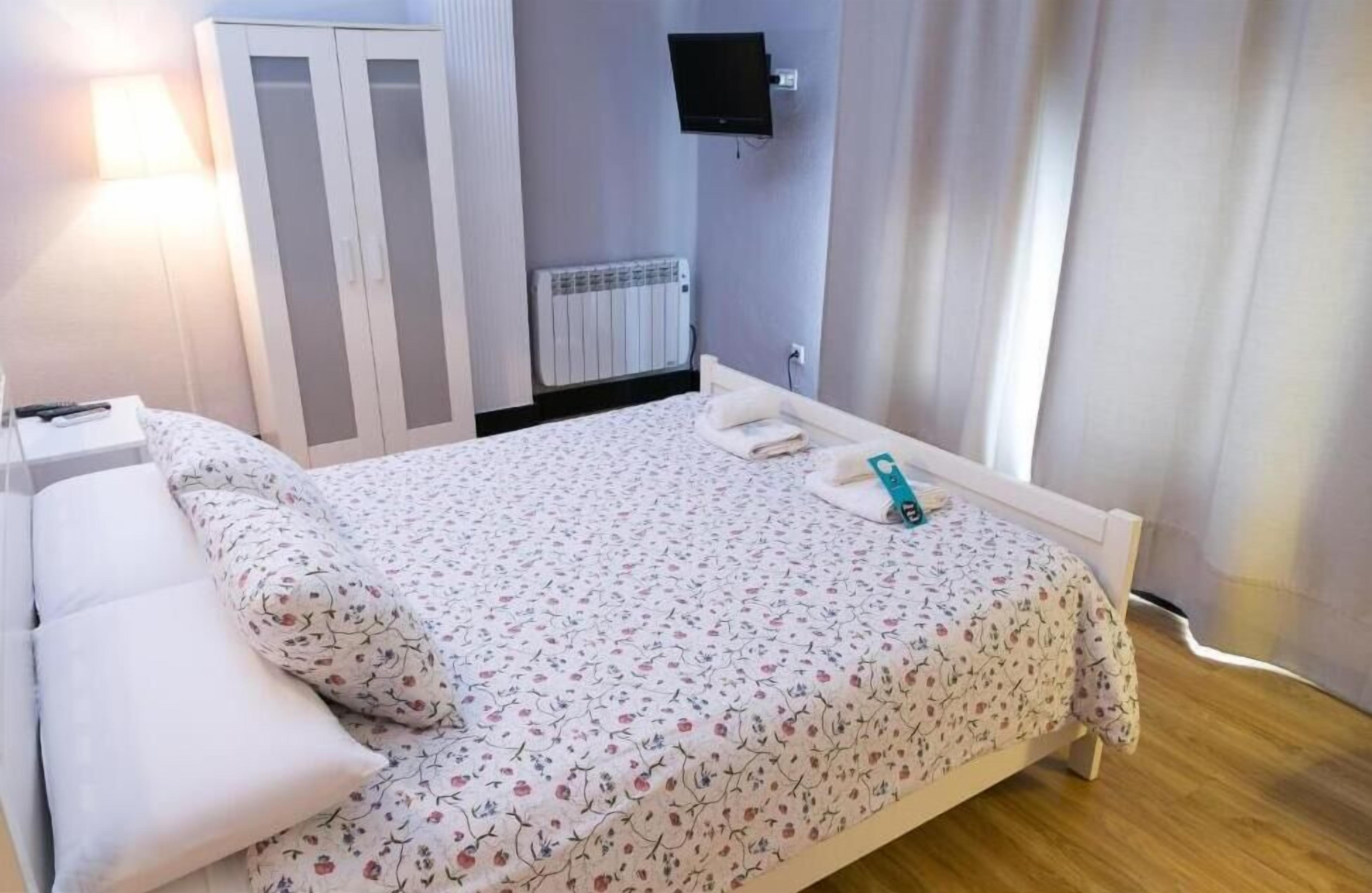 A bedroom with a bed, a nightstand, a wardrobe, a TV, and a radiator.