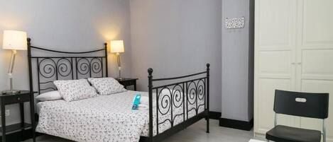 Un dormitorio con cama, dos mesitas de noche, una silla, un escritorio y un armario.