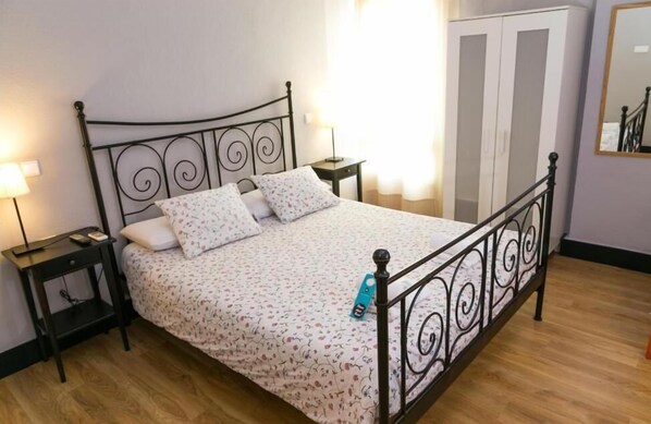 Una cama con estructura metálica, una mesita de noche con lámpara y un armario en una habitación con suelo de madera.