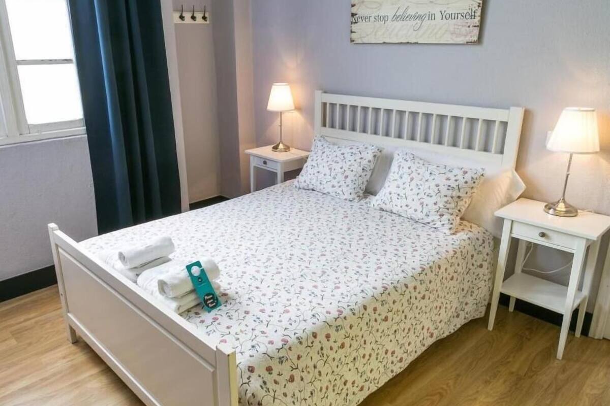 A neatly made bed with floral bedding, two bedside tables with lamps, and a motivational quote on the wall.