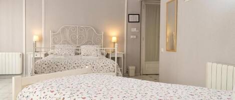 A bedroom with two beds, a white headboard, bedside tables, a radiator, a mirror, and a framed picture on the wall.