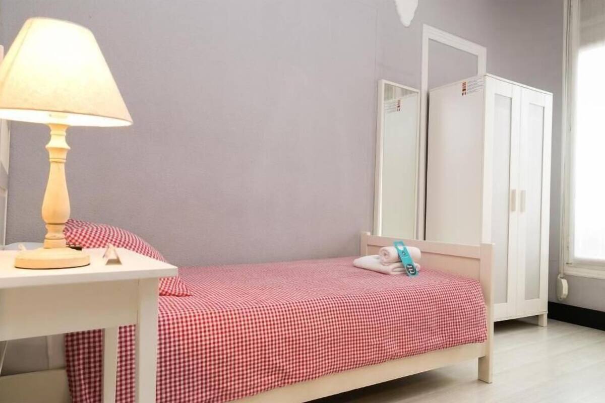 A small bedroom with a single bed, a nightstand, a lamp, and a wardrobe.