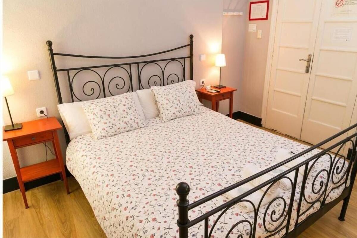A single bed with a floral bedspread, a nightstand with a lamp, and a door with a sign.