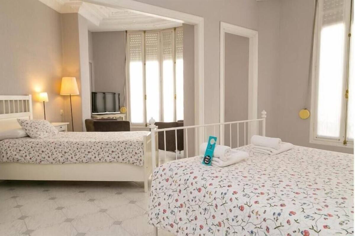 A hotel room with two beds, a TV, a desk, and a window with blinds.