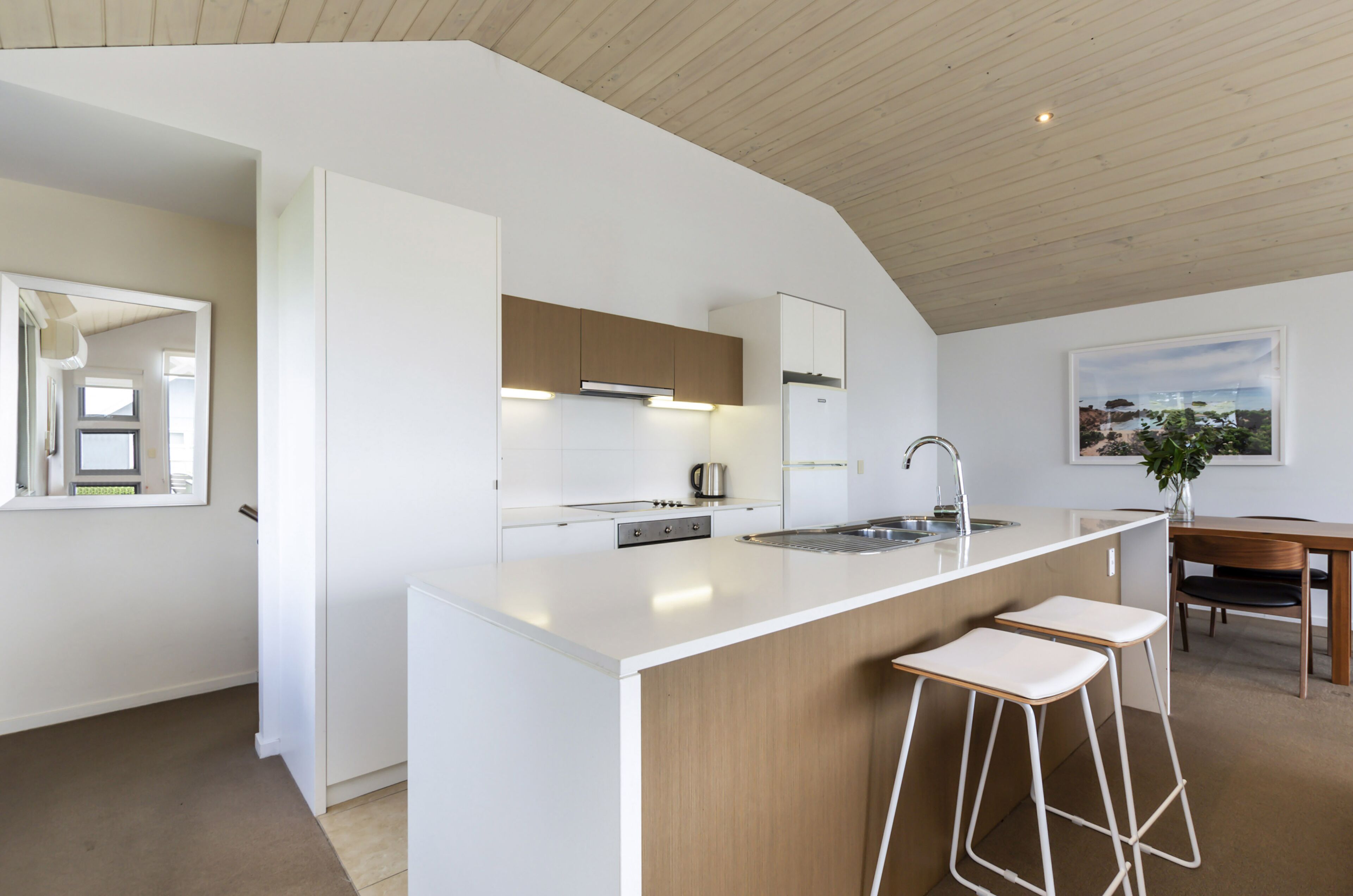A modern kitchen with white cabinetry, a central island with bar stools, and a view of the sea through a large window.