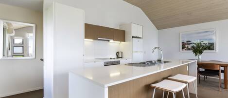 A modern kitchen with white cabinetry, a central island with bar stools, and a view of the sea through a large window.