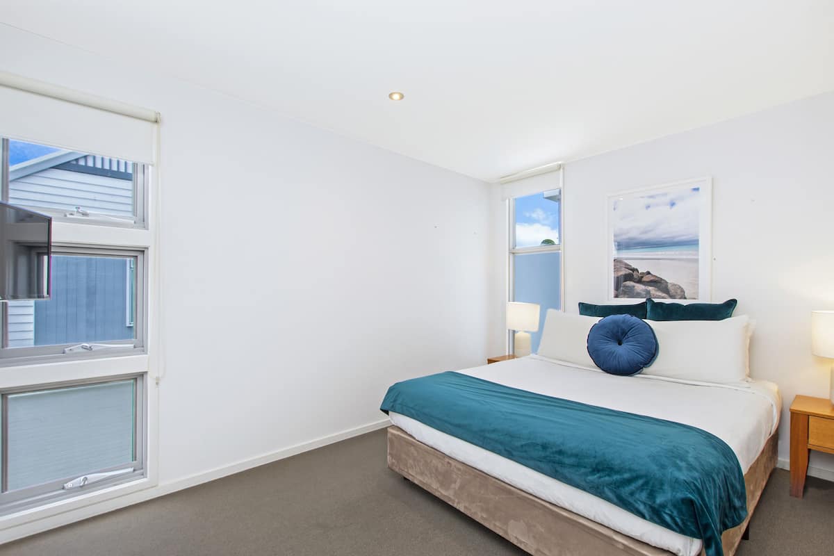 A bedroom with a bed, a window, a nightstand, and a wall-mounted lamp.