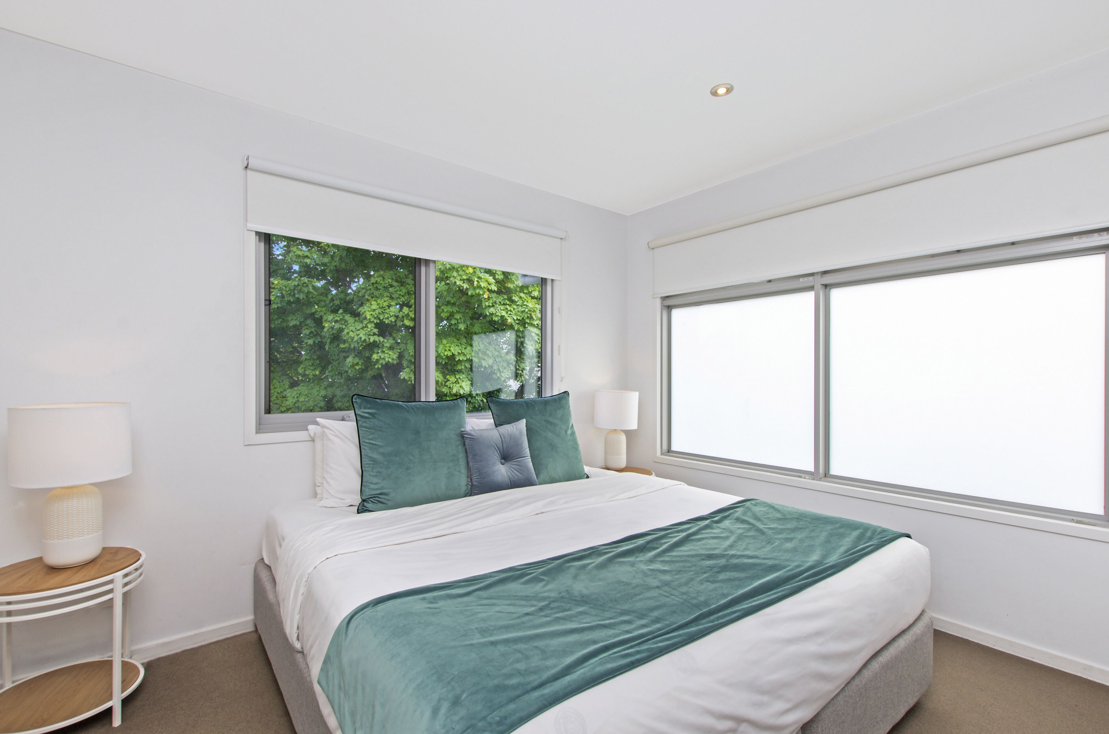 A bedroom with a large bed, two bedside tables, and a window with a view of trees.