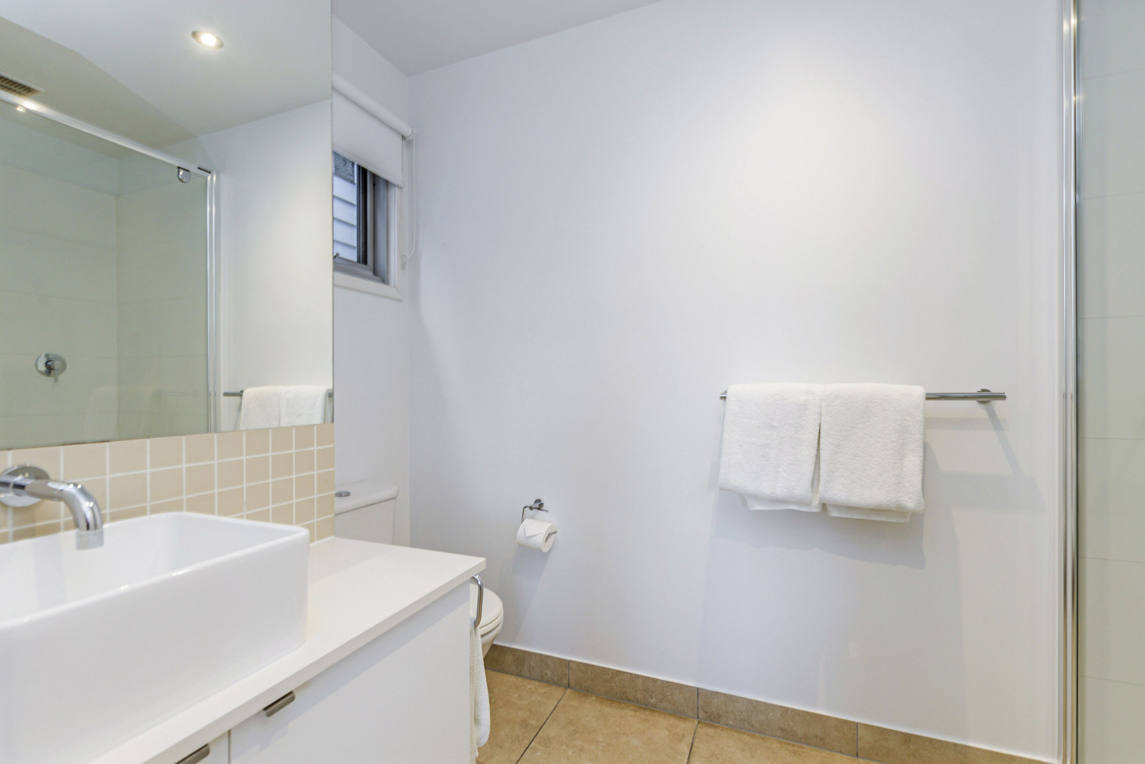 A modern bathroom with a white sink, mirror, and shower.