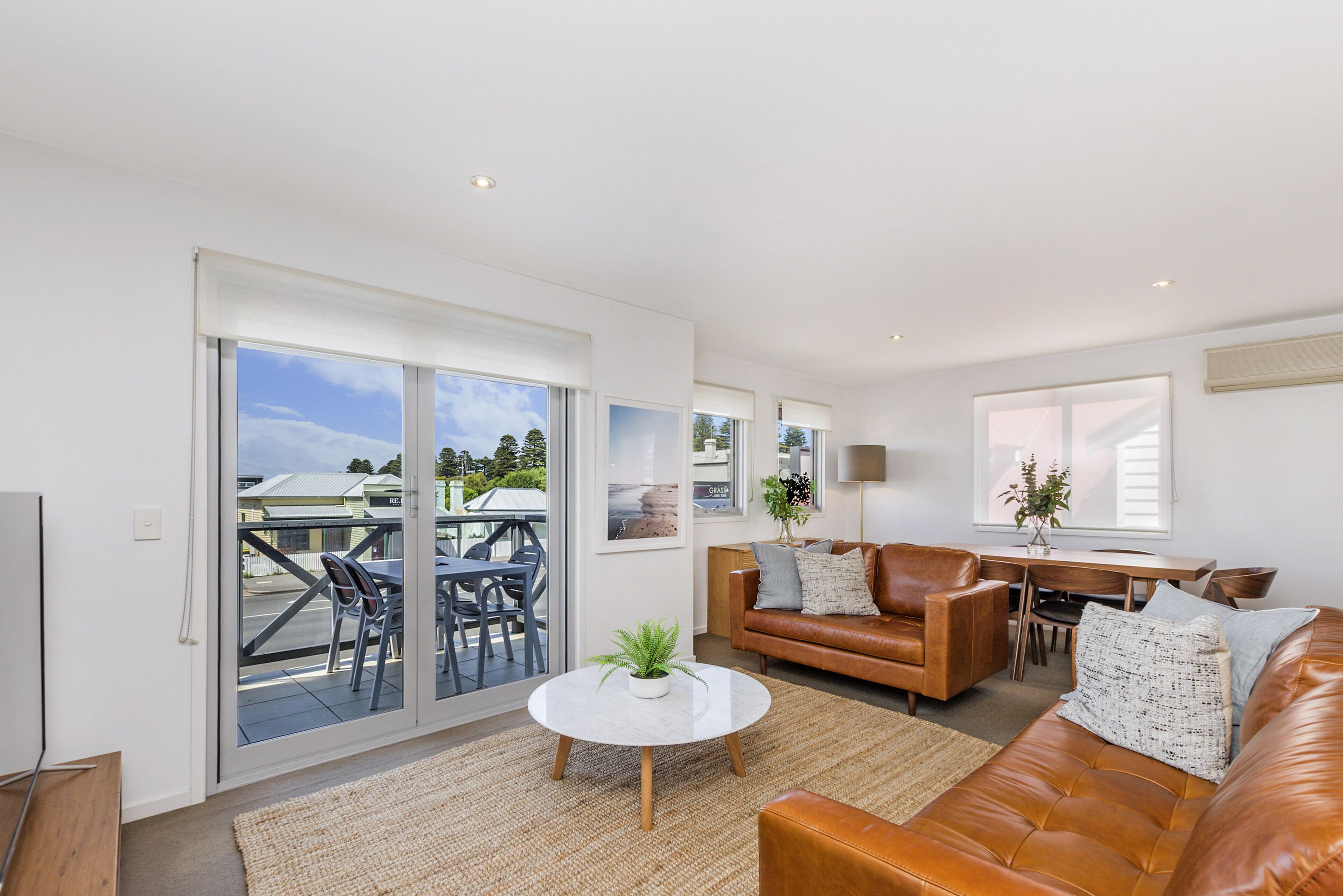 A modern living room with a leather sofa, a round coffee table, and a dining area with a table and chairs.