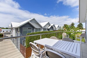 A balcony with a white table and chairs, overlooking a row of modern houses with grey roofs and white walls.