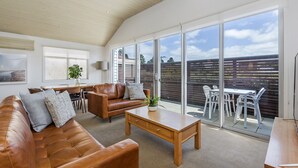 Un vaste espace de vie comprenant un canapé en cuir, une table basse en bois et une table à manger avec des chaises. De grandes fenêtres offrent une vue sur le jardin.