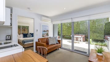 Una habitación moderna con cama, un sofá de cuero marrón, una mesa de comedor de madera y un amplio ventanal corredero que da a un patio exterior.