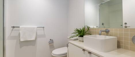 Un baño moderno con inodoro blanco, lavamanos con espejo y una planta en maceta.
