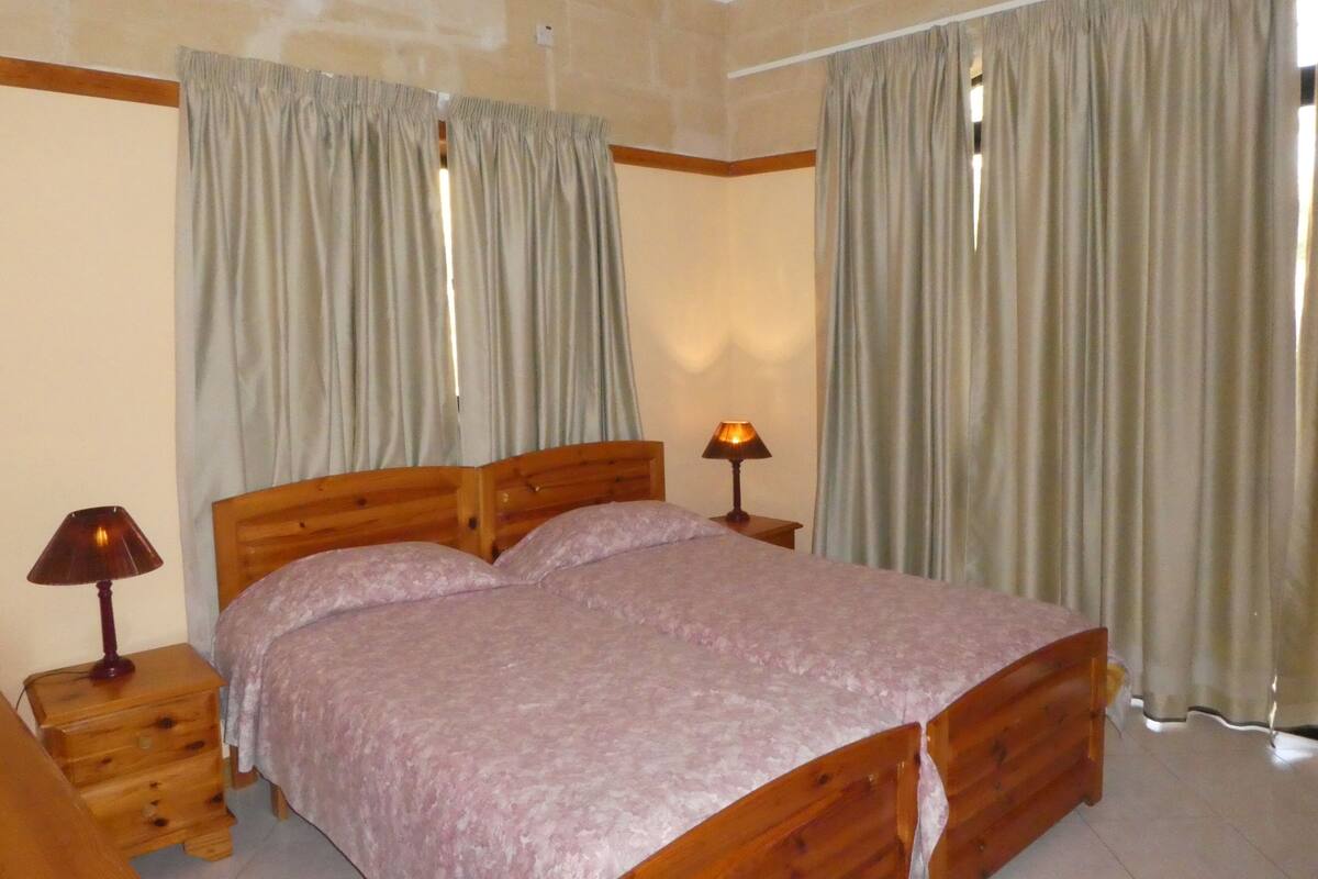 Une chambre à coucher avec un lit en bois, deux tables de chevet avec des lampes et des rideaux beiges.