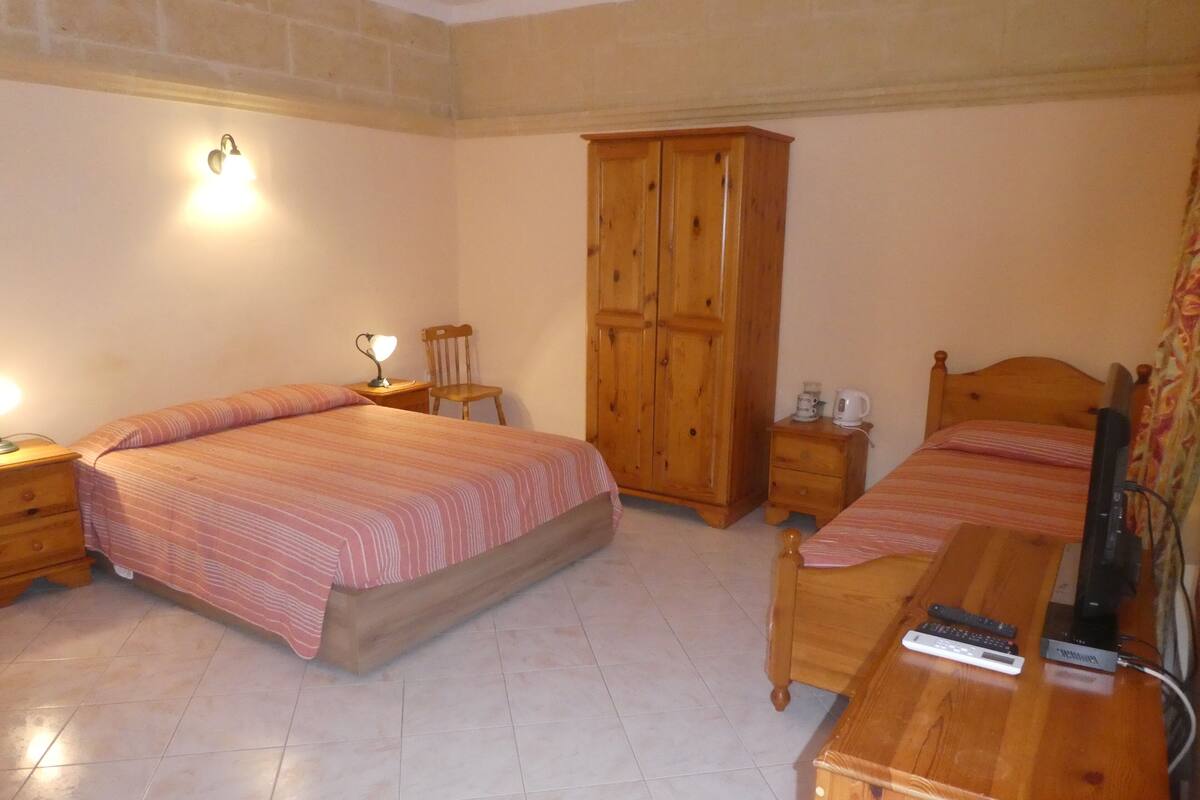 Une chambre avec deux lits, une armoire en bois, une table de chevet avec une lampe et un téléviseur.