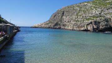 A coastal area with clear water, rocky cliffs, and a pier with people.