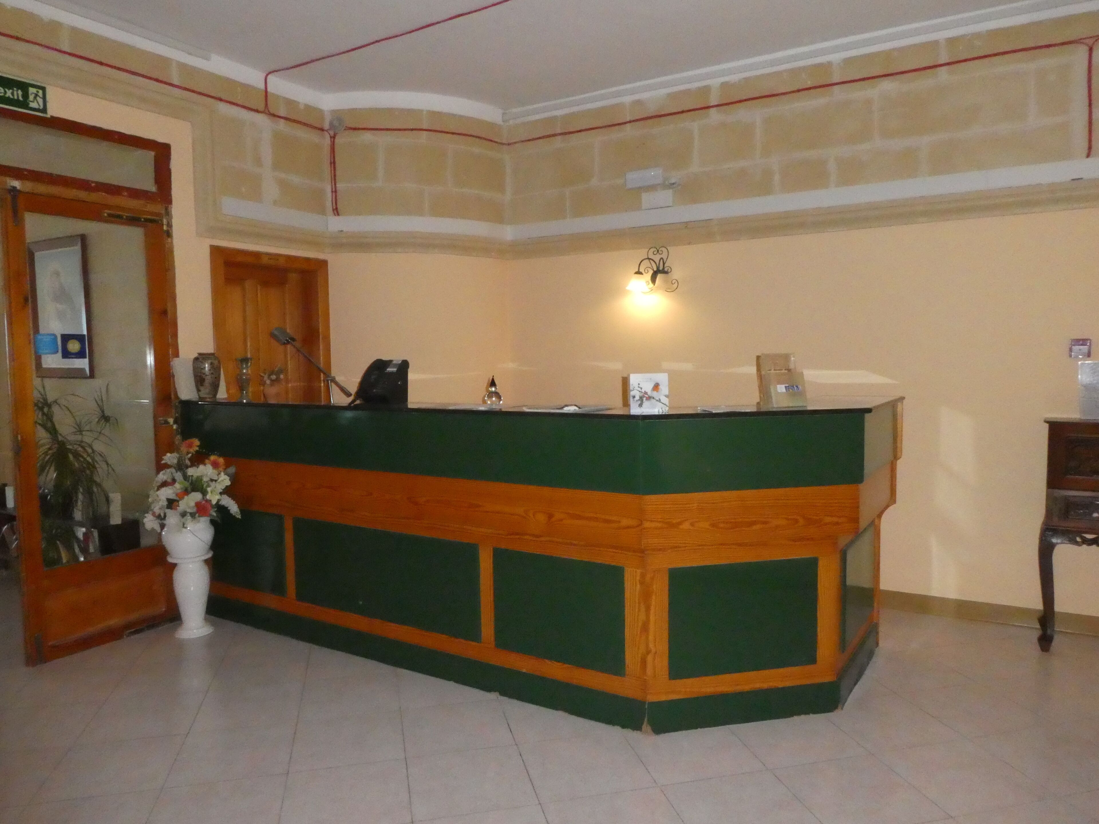A reception desk with a green and wooden design, a wall-mounted light, and a potted plant.