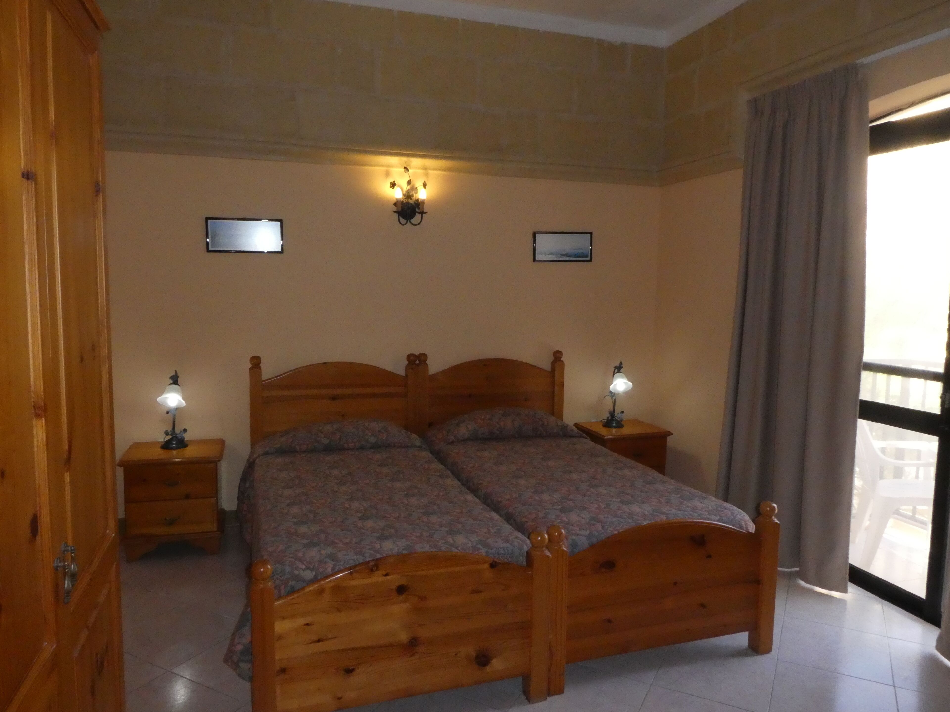 A double wooden bed with two bedside tables, each with a lamp, in a room with stone walls and a large window.