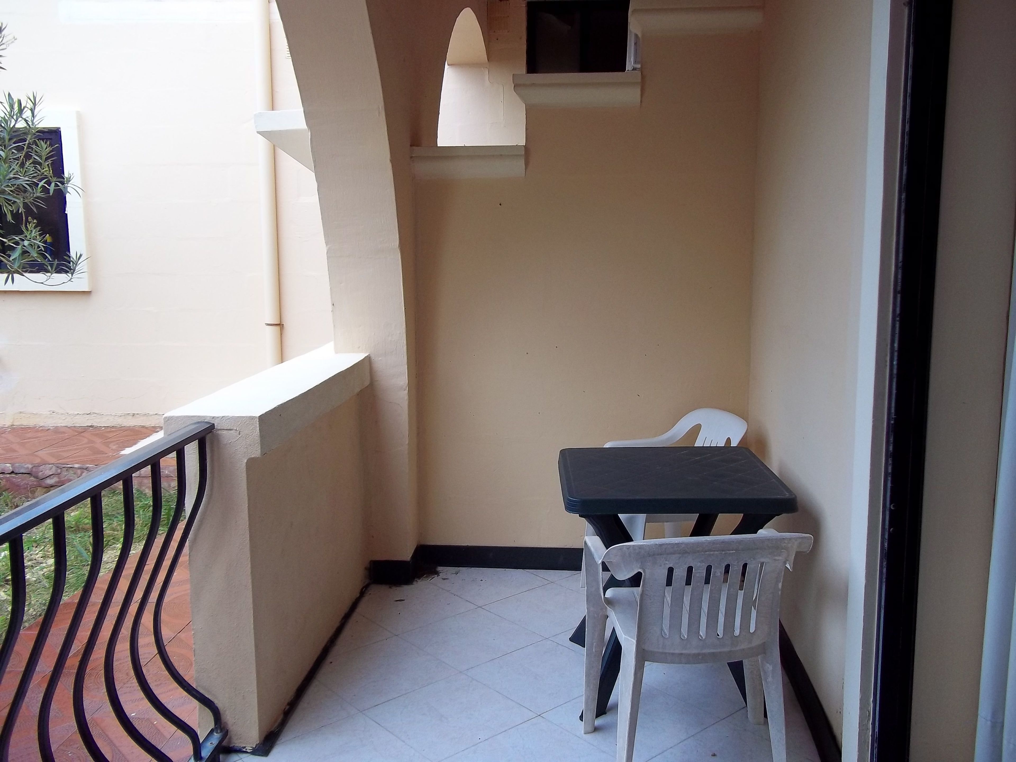 Un pequeño balcón con una mesa, dos sillas, barandilla y ventana con vista al exterior.