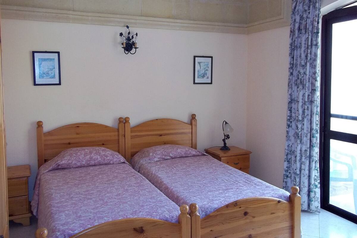 Une chambre à coucher avec un lit double, deux tables de chevet, une lampe fixée au mur et deux tableaux encadrés.