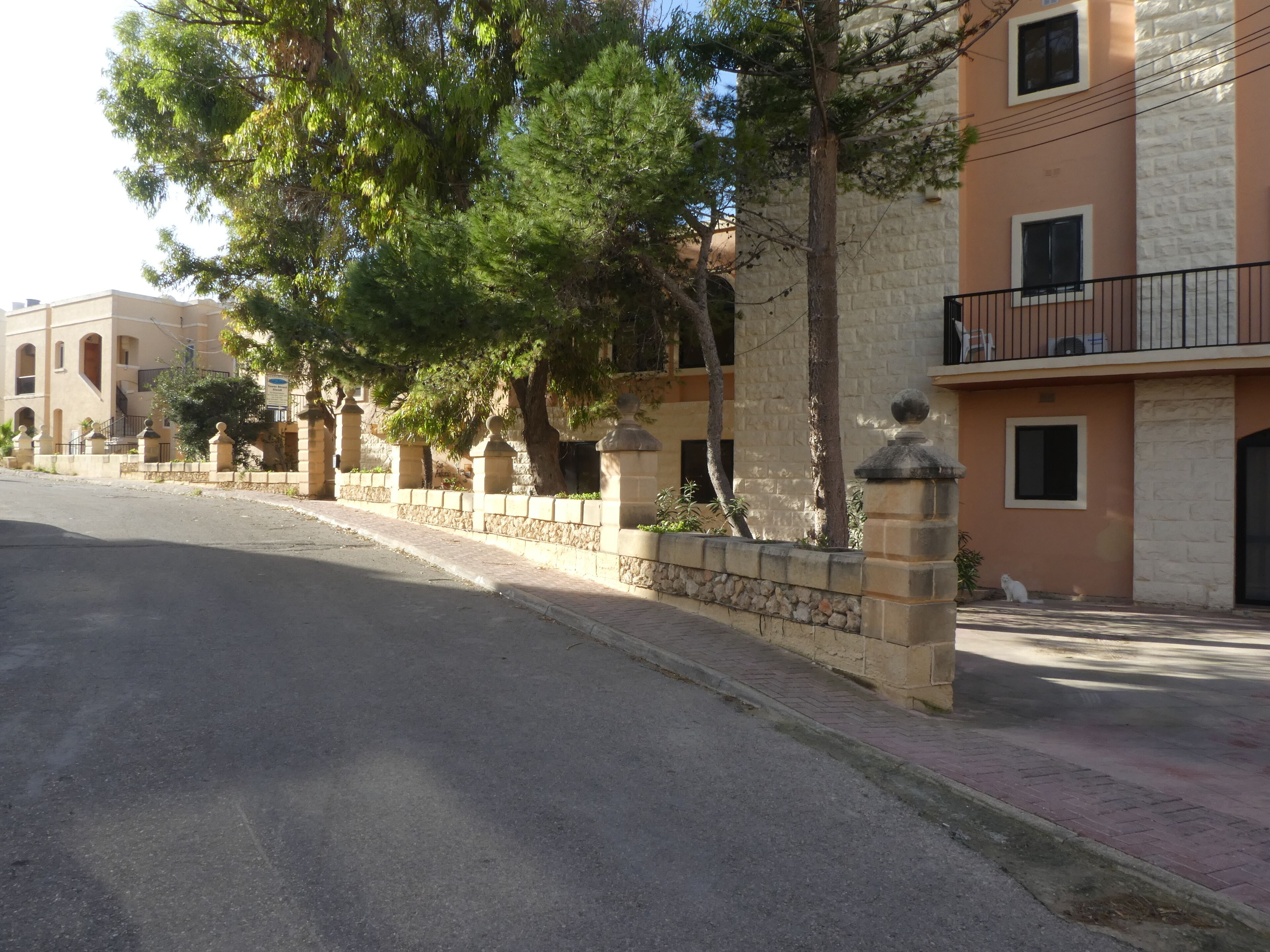 A street with a row of buildings, stone walls, and trees.