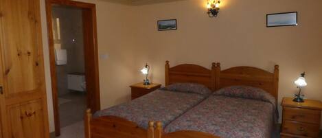 A bedroom with a wooden bed, two bedside tables with lamps, a wooden wardrobe, and a door leading to another room.