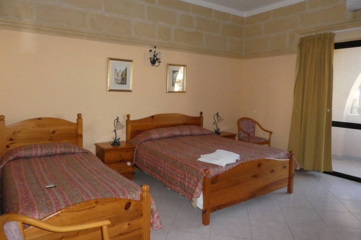 Une chambre à coucher avec deux lits en bois, une table de chevet, une chaise et une fenêtre avec des rideaux.