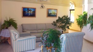 Un salon avec des canapés à rayures, deux tableaux de paysages encadrés et plusieurs plantes en pot.