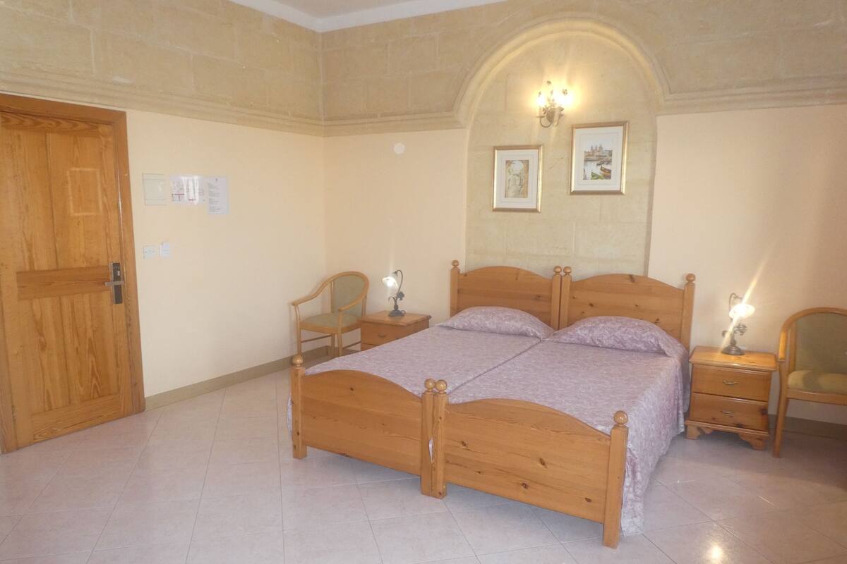 Une chambre à coucher avec un lit en bois, deux tables de chevet avec des lampes, une chaise et une porte.