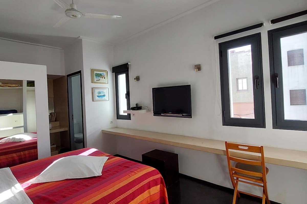 A hotel room with two beds, a desk with a TV, a chair, and a window.