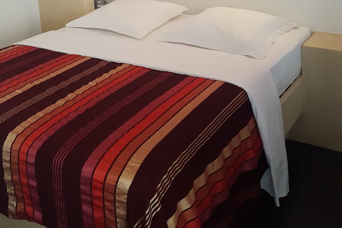 A bed with white linens and a striped blanket, a ceiling fan, and a wall-mounted light fixture.