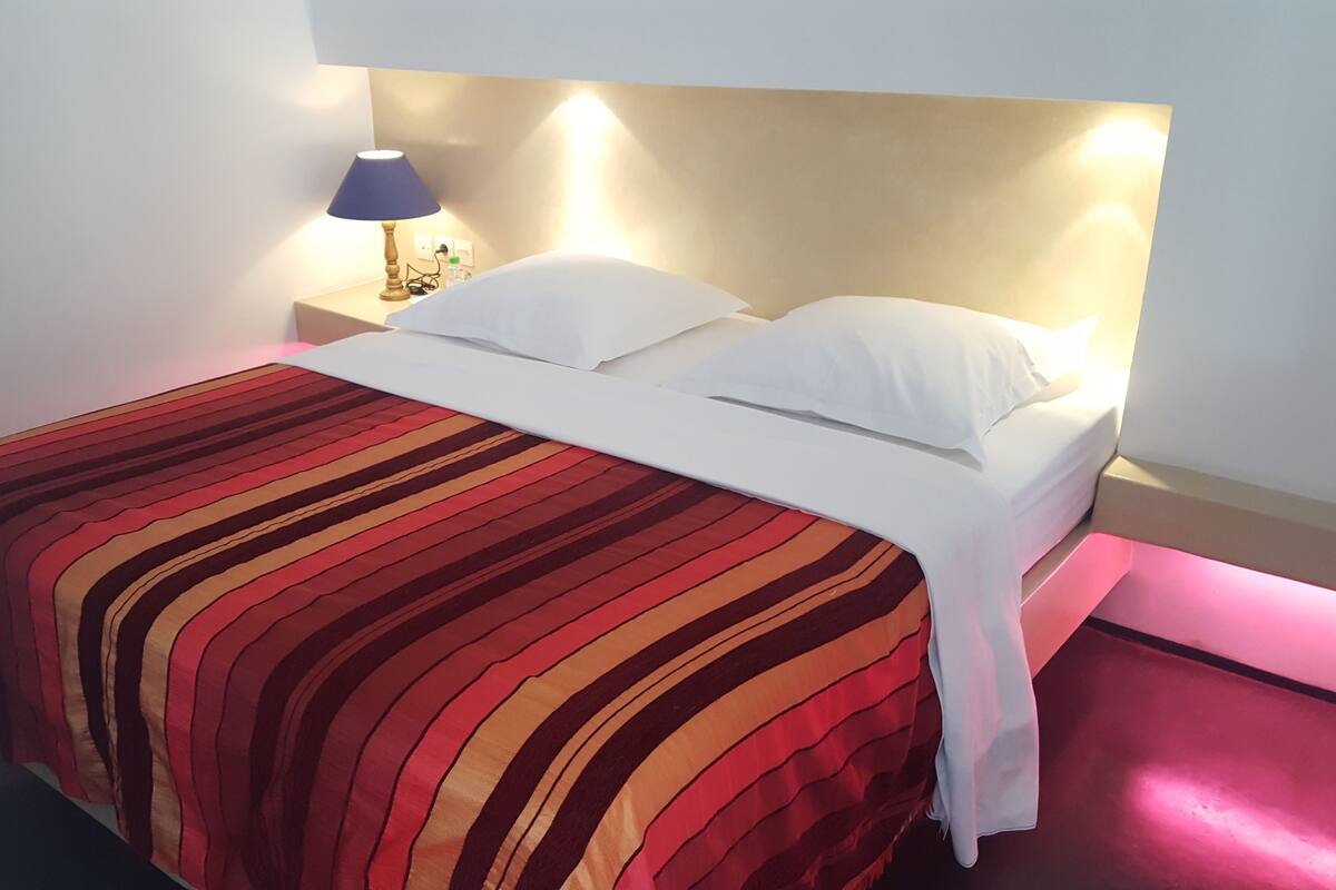 A neatly made bed with a striped bedspread, a bedside lamp, and a wall-mounted light fixture.