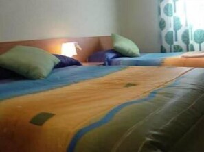 Una habitación de hotel con dos camas, cada una con una colcha azul y naranja, y almohadas verdes.