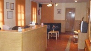A reception area with a wooden reception desk, a small table with a vase, a sofa, and a television. - Hostal Emilio (Madrid)