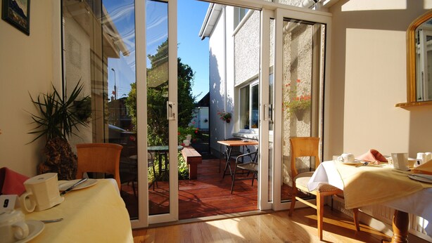Une pièce dotée d’une porte-fenêtre coulissante donnant sur un patio extérieur, d ’une table à manger avec des chaises, et d’une petite table recouverte d’une nappe, avec des tasses.