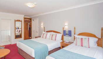 Una habitación de hotel con dos camas, un armario de madera, un espejo y una mesita.