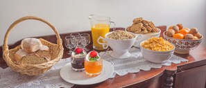 Une table de petit-déjeuner avec du pain, des céréales, des oranges et une carafe de jus d’orange.