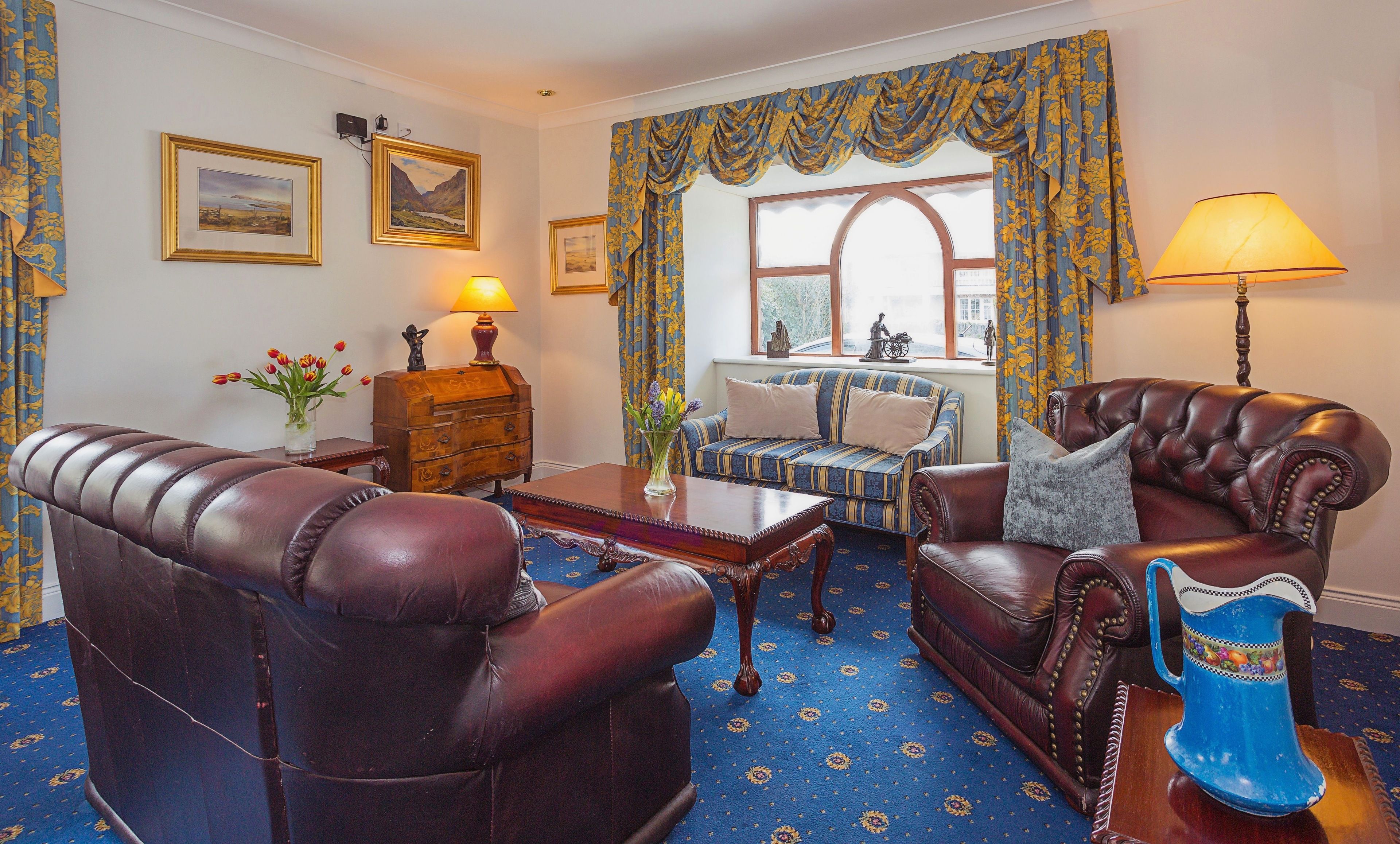 A traditional room with leather armchairs, a sofa, a wooden cabinet, and a blue patterned carpet.