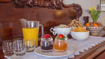 A breakfast setting with a pitcher of orange juice, a plate with two glasses of tea, and bowls of cereal and fruits.