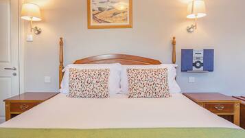 A neatly made bed with two pillows, a bedside table, a wall-mounted lamp, and a framed picture above the bed.