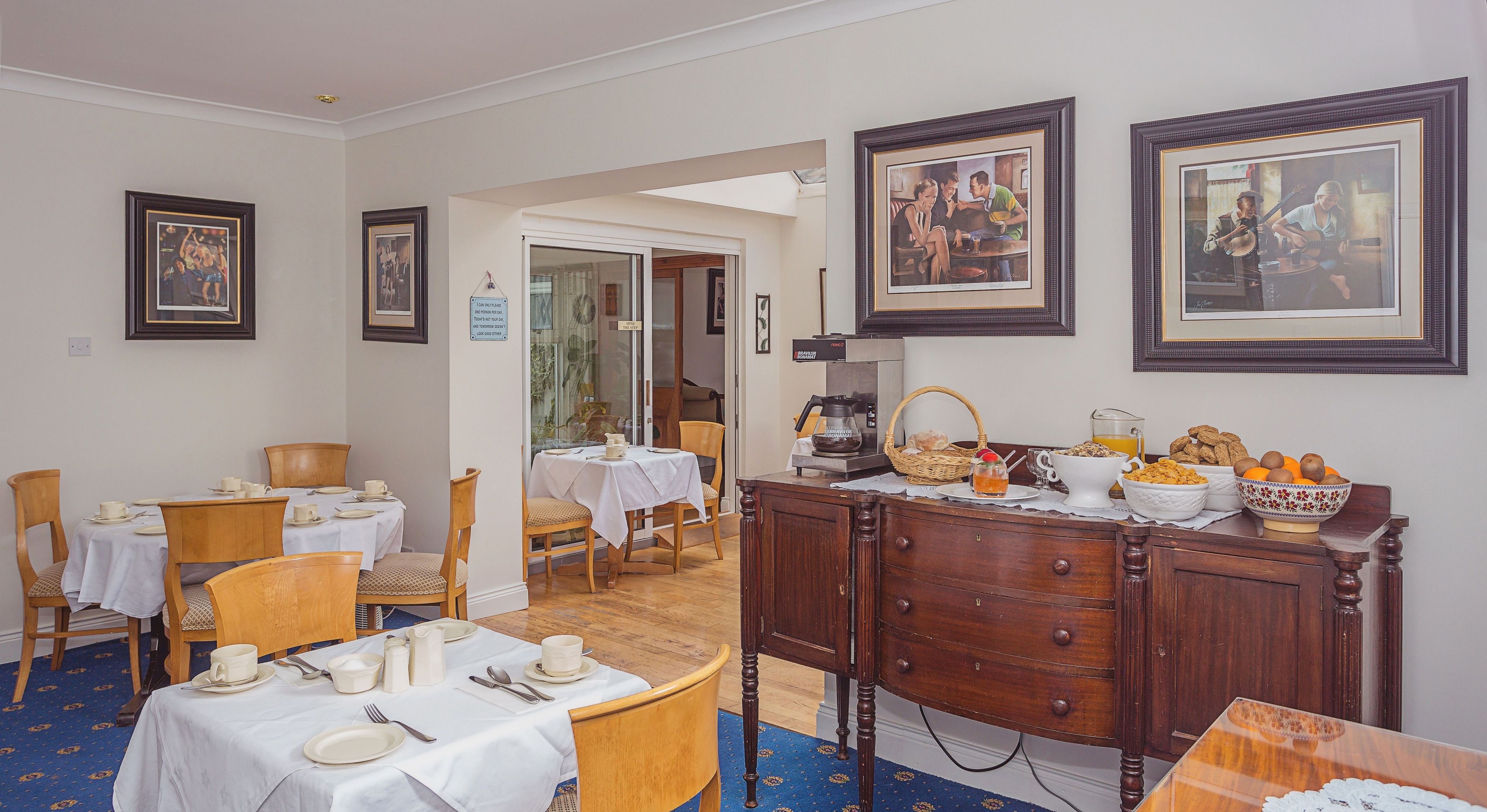 A dining area with tables set for breakfast, a coffee station, and framed artwork on the walls.