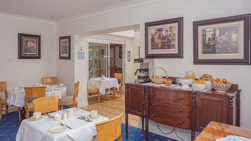 A dining area with tables set for breakfast, a coffee station, and framed artwork on the walls.