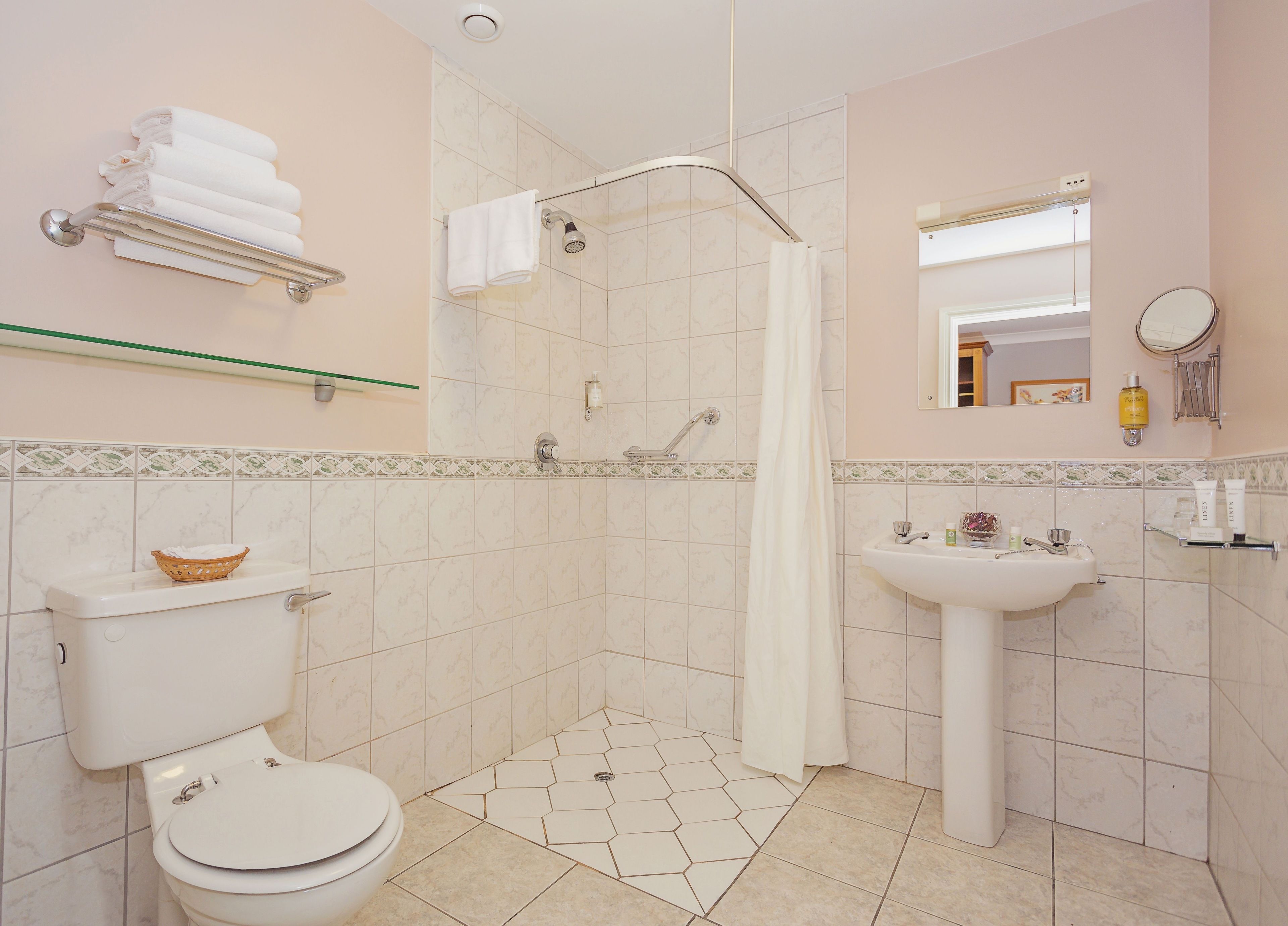 A bathroom with a toilet, shower, sink, and a mirror.