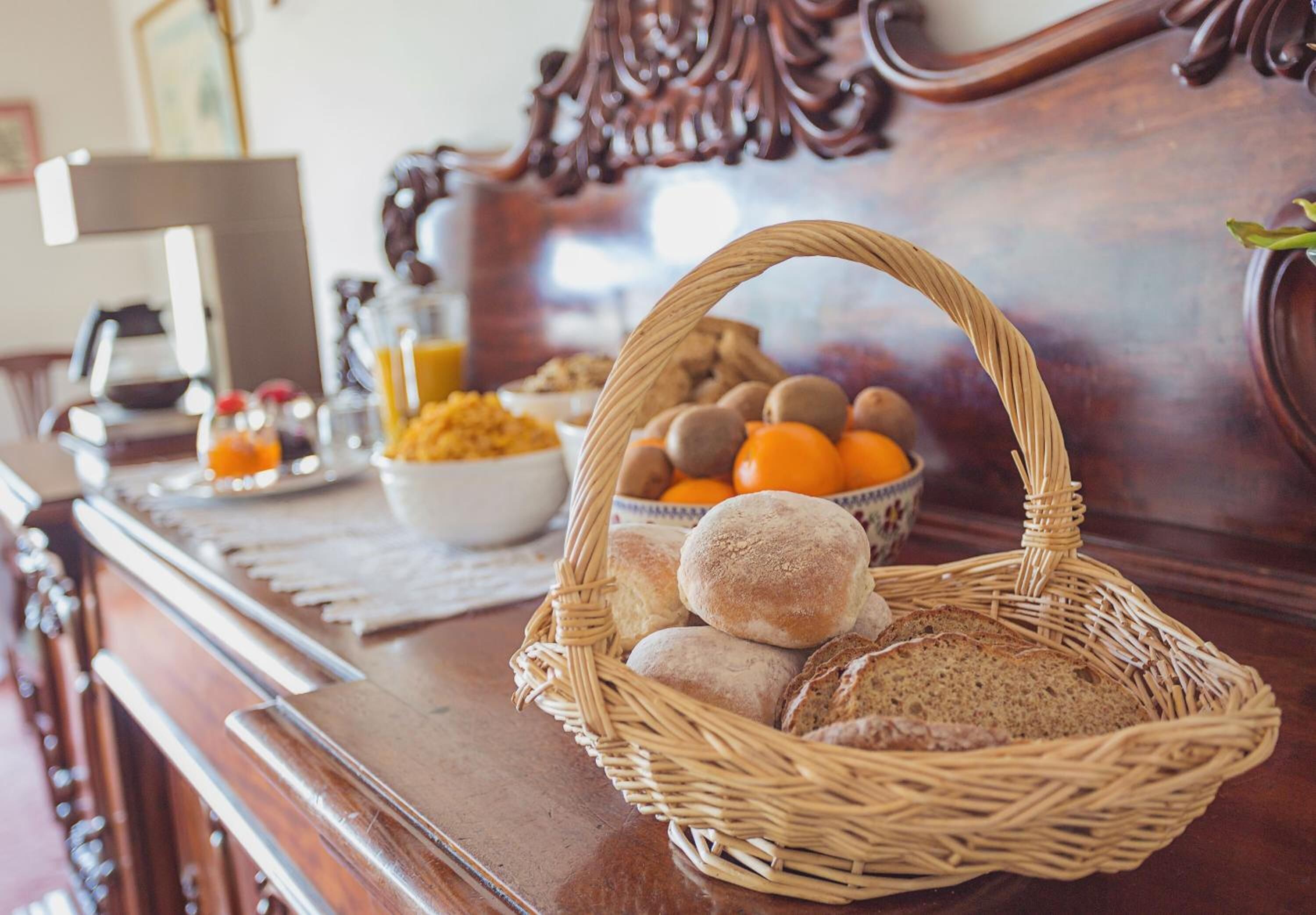 A wicker basket filled with bread and oranges on a wooden table.