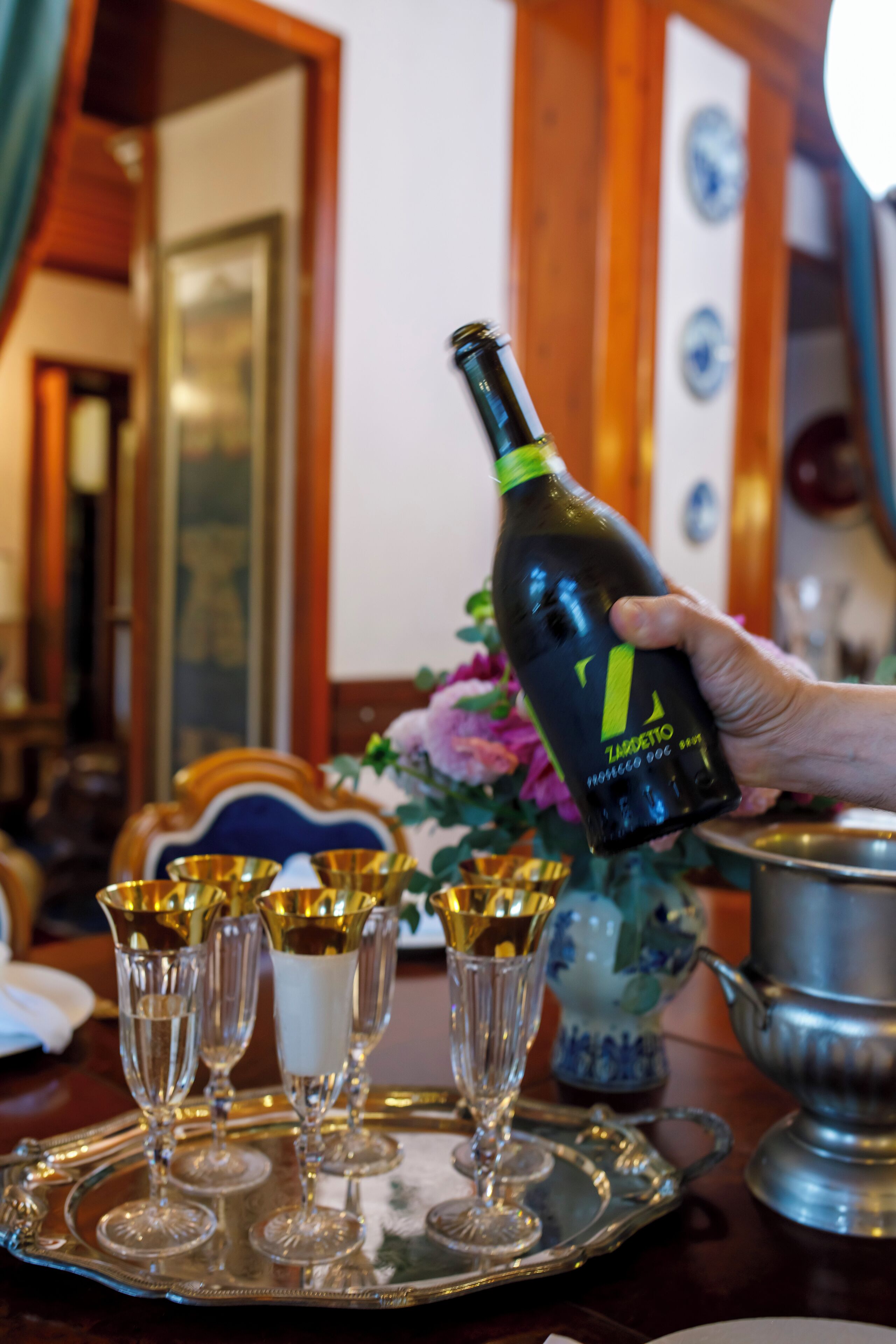 A hand holding a bottle of wine with a label, placed on a tray with several wine glasses.