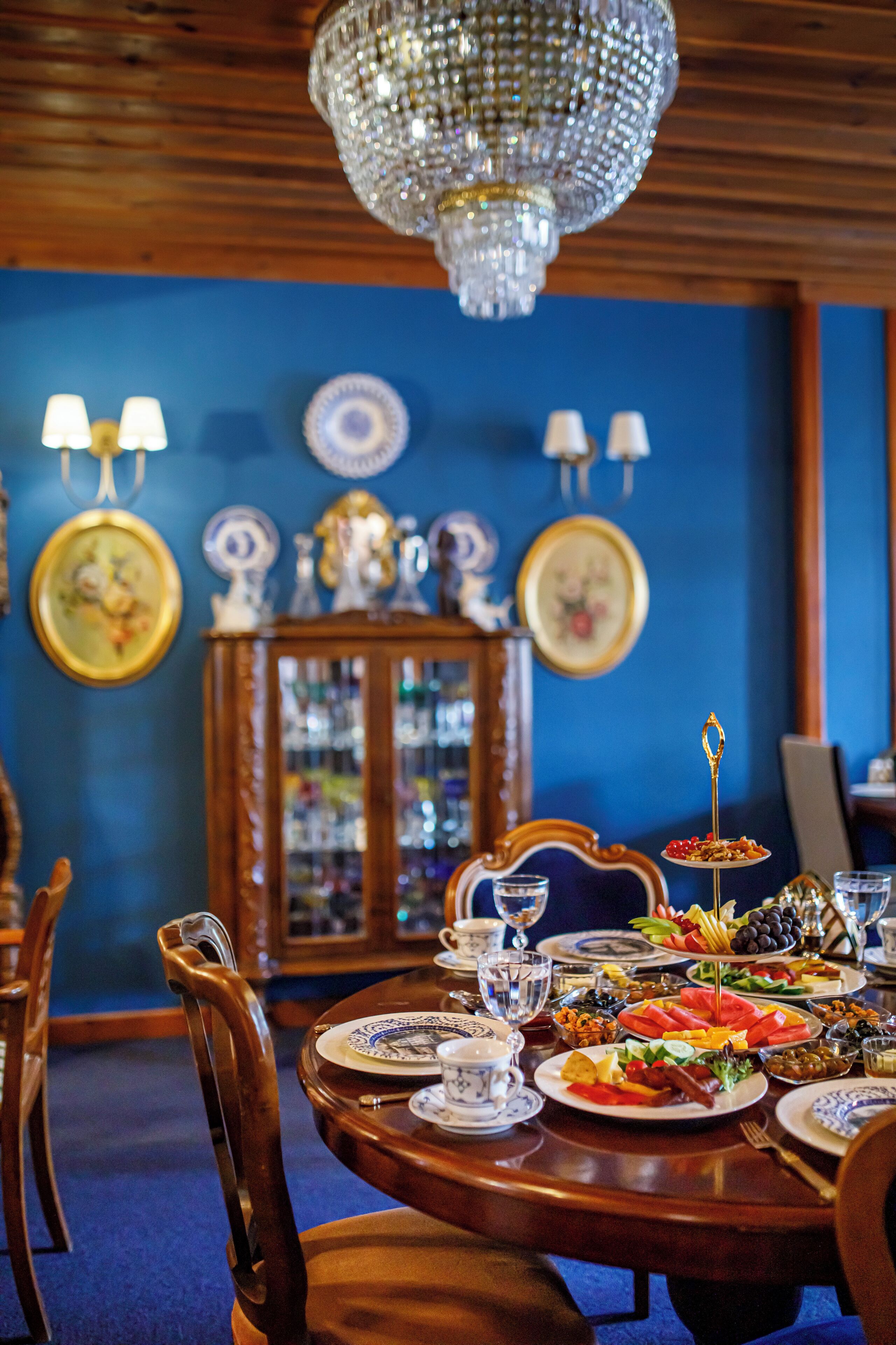 Zona pranzo con tavolo di legno apparecchiato per un pasto, circondato da sedie. Un lampadario pende dal soffitto e ci sono lampade a parete.